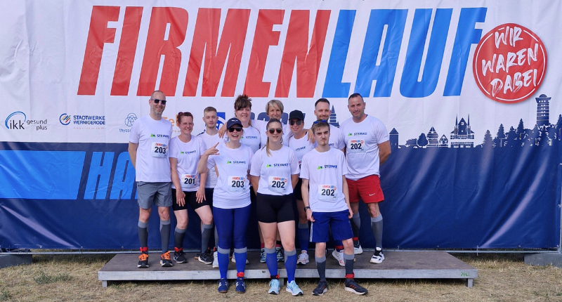 Gruppenbild vom Harzer Firmenlauf: 12 Teammitglieder von Steinke stehen vor Wand mit der Aufschrift "Firmenlauf - Wir waren dabei"